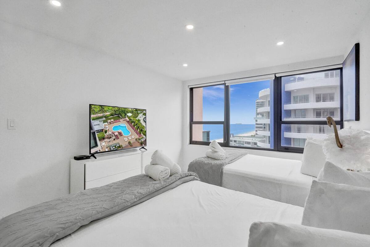 Quarto de hotel moderno com uma janela grande que oferece vista para uma piscina e prédios.