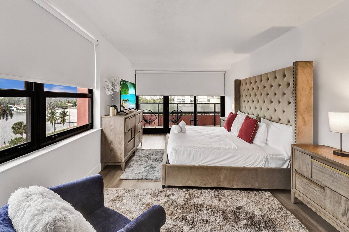 Quarto moderno com uma cama grande, vista para o mar, cômoda de madeira e uma cadeira.