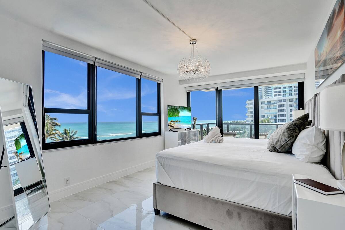 Quarto moderno com uma cama grande, uma televisão e vista para o mar.