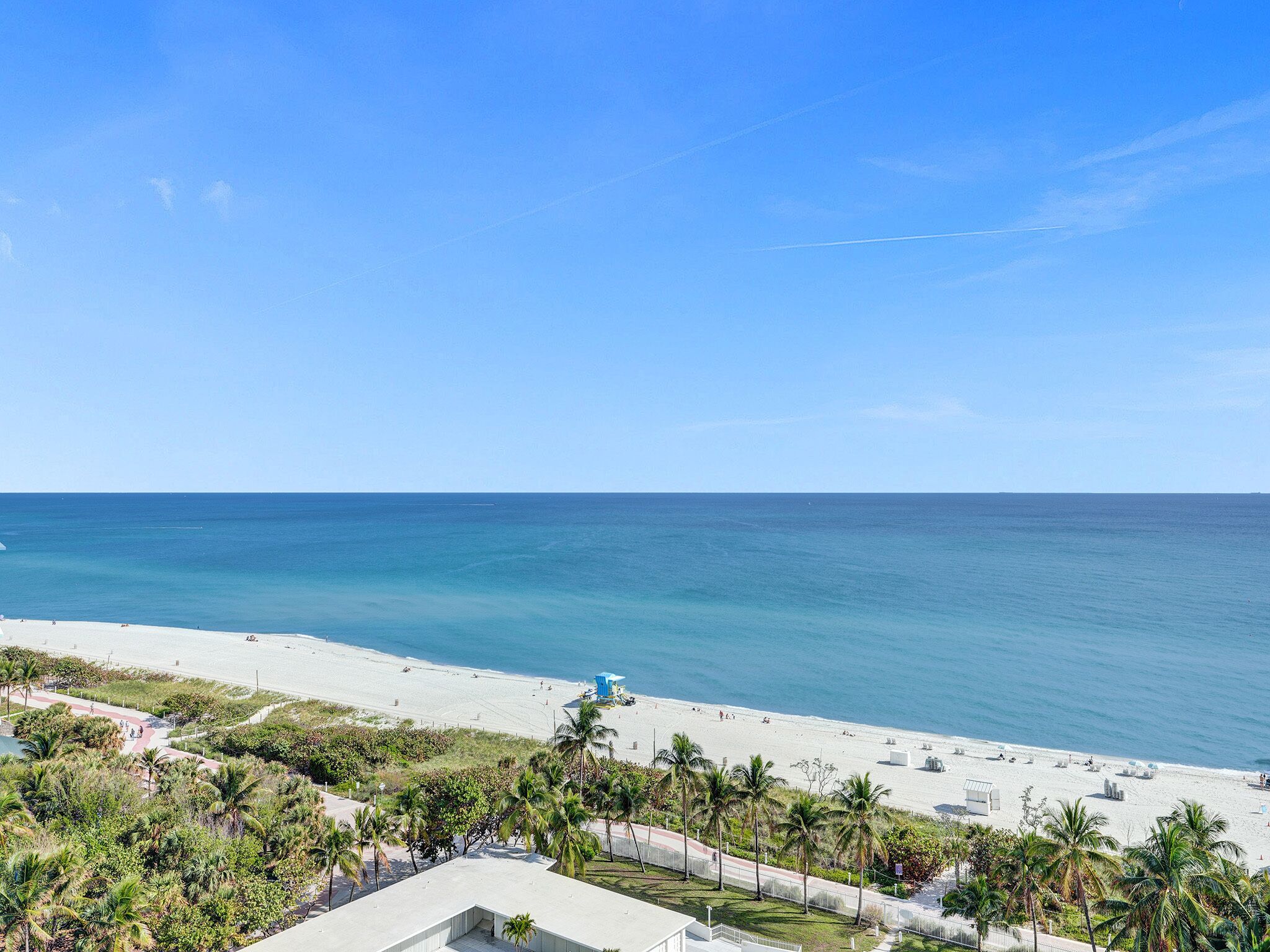 Blick auf einen Strand mit blauem Himmel, Palmen und feinem Sand.