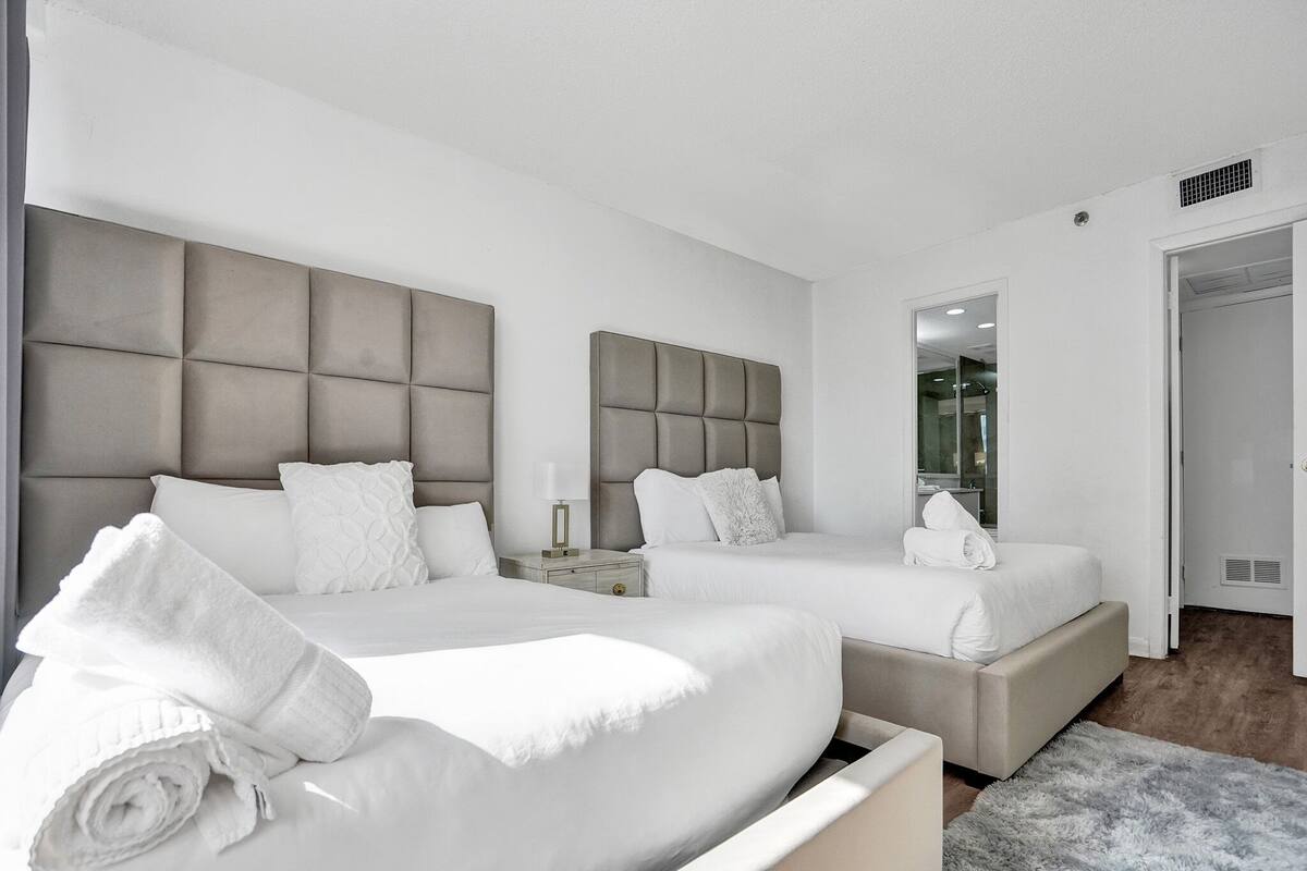 Quarto de hotel moderno com duas camas, um espelho grande e um closet espaçoso.