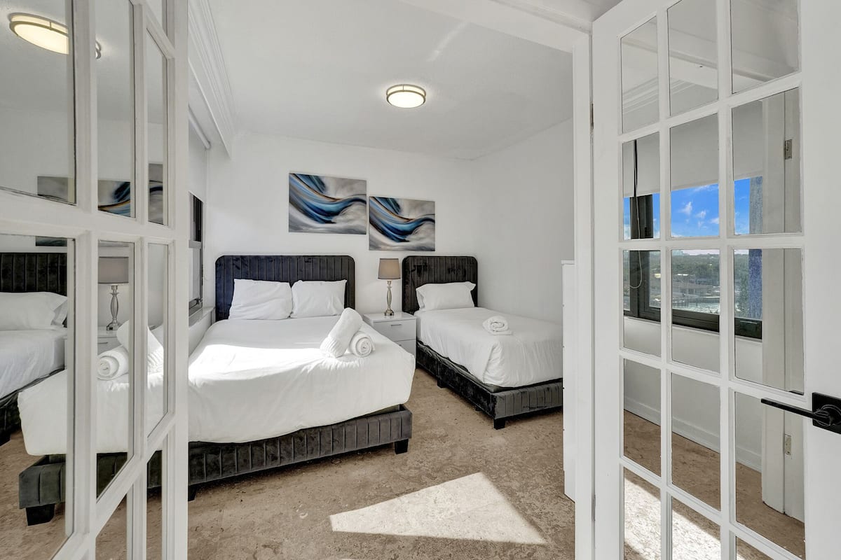 Quarto de hotel com uma cama grande, duas camas menores e vista através de uma porta de vidro.