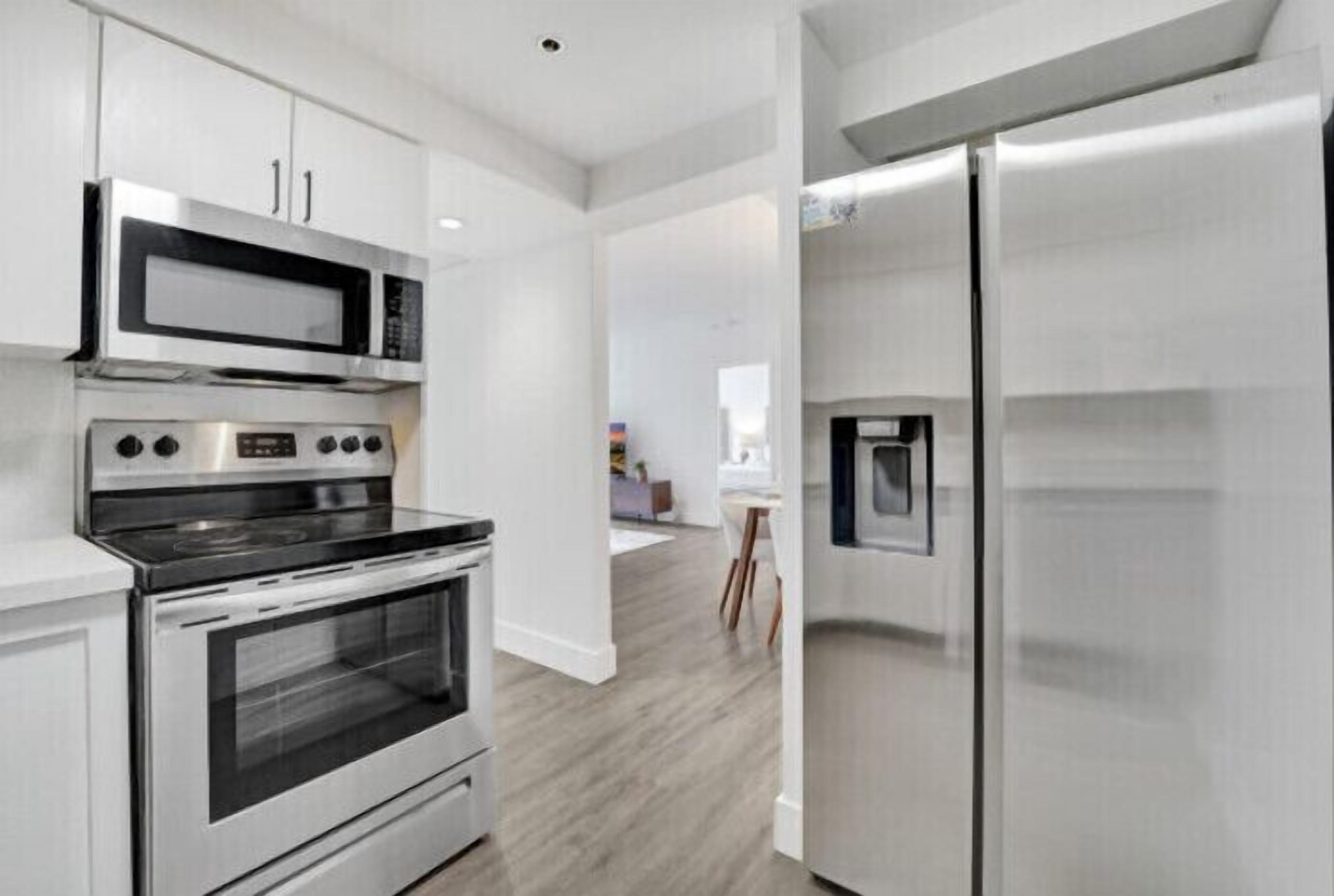 A modern kitchen with stainless steel appliances, white cabinetry, and a wooden floor.
