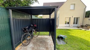 A covered bike parking area with a bicycle and a green lawn in the background. - Ecrin de charme (Compiègne)