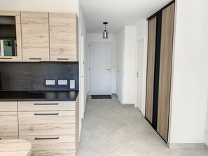 A narrow hallway with a kitchen area on the left, featuring wooden cabinets and a black countertop. - Ecrin de charme (Compiègne)