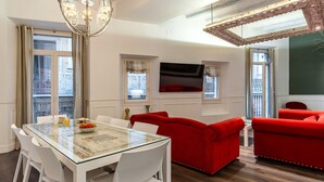 A modern living room with a glass-top dining table, white chairs, and red sofas. - Enjoybcn Tallers Apartment (Barcelona)