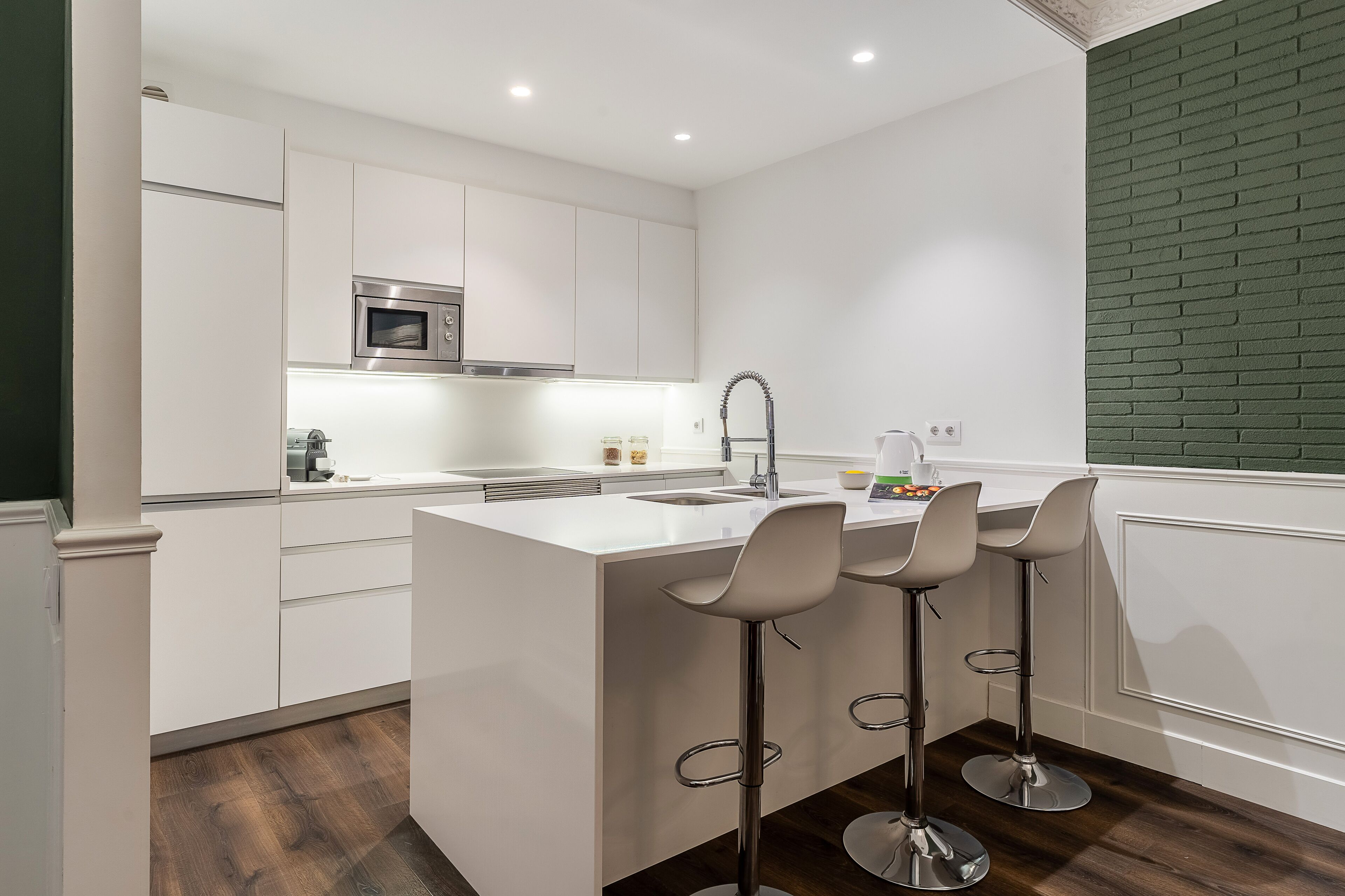 Una cocina moderna con armarios blancos, una isla central con taburetes de bar, un lavamanos de acero inoxidable y un microondas.