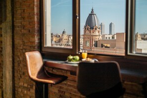 Un espace repas comprenant une table et des chaises, une fenêtre donnant sur un paysage urbain avec, notamment, un bâtiment imposant surmonté d’un dôme.