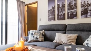 En moderne stue med en grå sofa, to lys i en bakke, og tre bybilleder hængende på væggen.