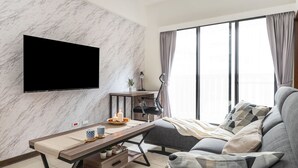En moderne stue med en marmorvæg, et fladskærms-tv, et skrivebord med lampe, en sofa og store vinduer med gardiner.