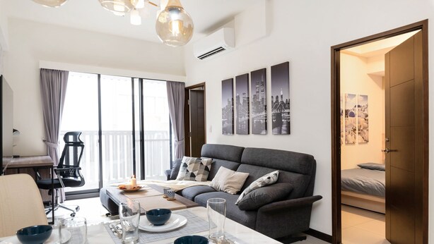 En moderne stue med sofa, spisebord dækket til to personer, og en balkon med udsigt.