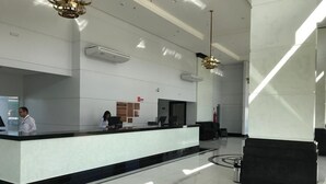 A modern hotel lobby with a reception desk, two employees, a large geometric floor design, and a chandelier. - Piazza diRoma Acesso Acqua Park (Caldas Novas)