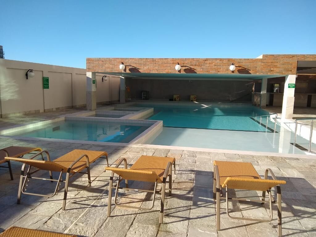 A swimming pool with multiple lanes, surrounded by lounge chairs and a brick wall.
