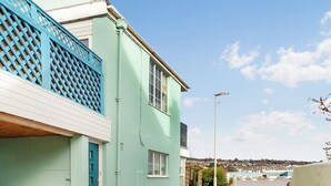 Un vicolo stretto con un edificio azzurro tenue, un recinto in traliccio blu e vista su un porto con barche.