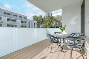 Eine moderne Außenpatio mit einem runden Tisch und Stühlen, einem Topfpflanzen und Blick auf ein Gebäude mit Balkonen und Bäumen.