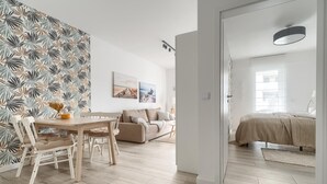 A modern living room with a wooden dining table, beige sofa, and a bed with a beige bedspread. - Apartment in Rewal near Baltic Sea Beach (Rewal)