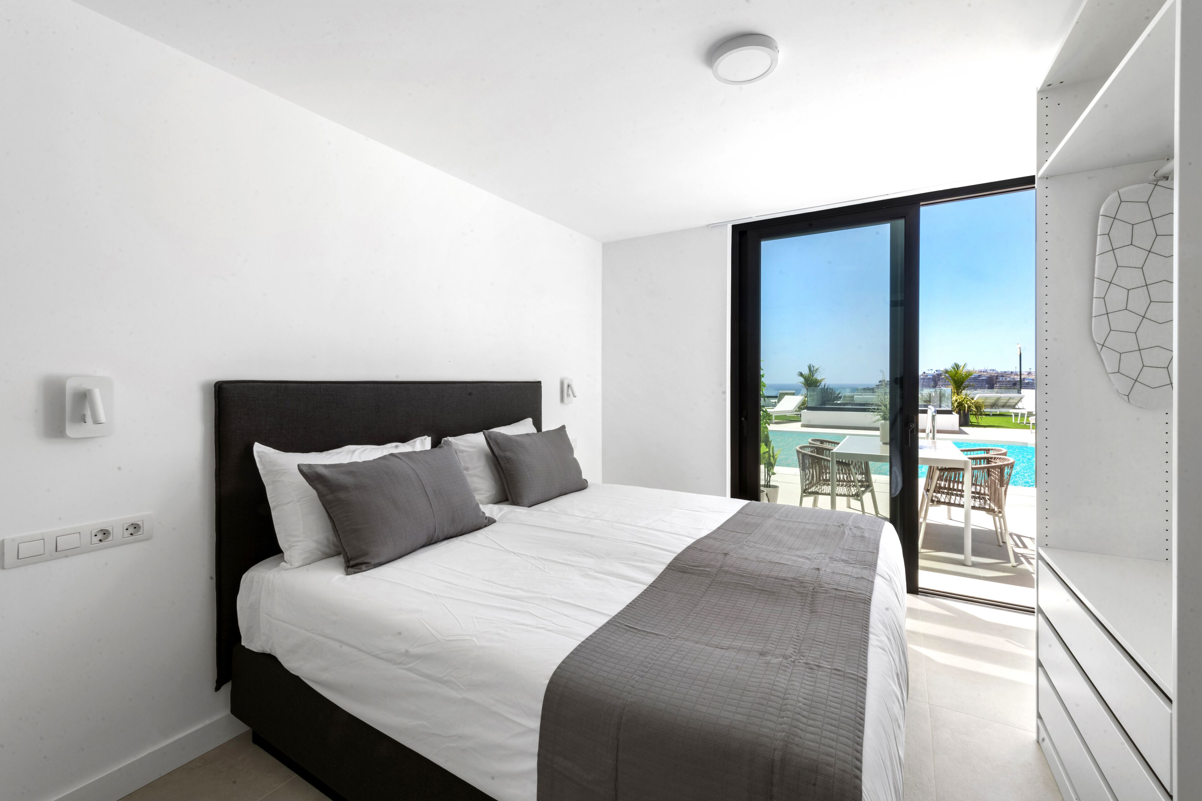 Une chambre moderne avec un grand lit, des murs blancs et une vue sur un espace piscine extérieur.