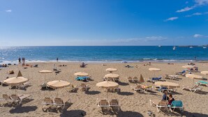 A beach with rows of sun loungers and umbrellas, a clear blue sky, and calm sea. - Palmera Sea View (Mogan)