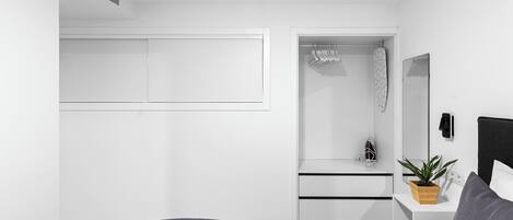A modern bedroom with a bed, a bedside table with a plant, a wardrobe, and a mirror.
