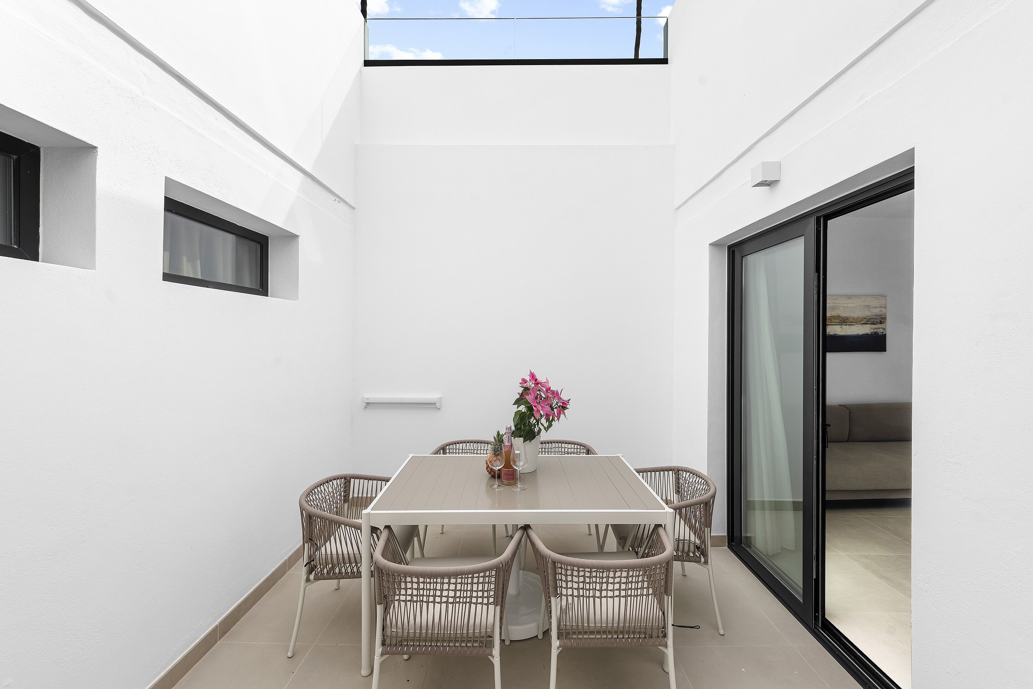 Ein heller Innenraum mit Tisch und Korbstühlen, einem kleinen Blumentopf und einer Glastür zum Balkon.