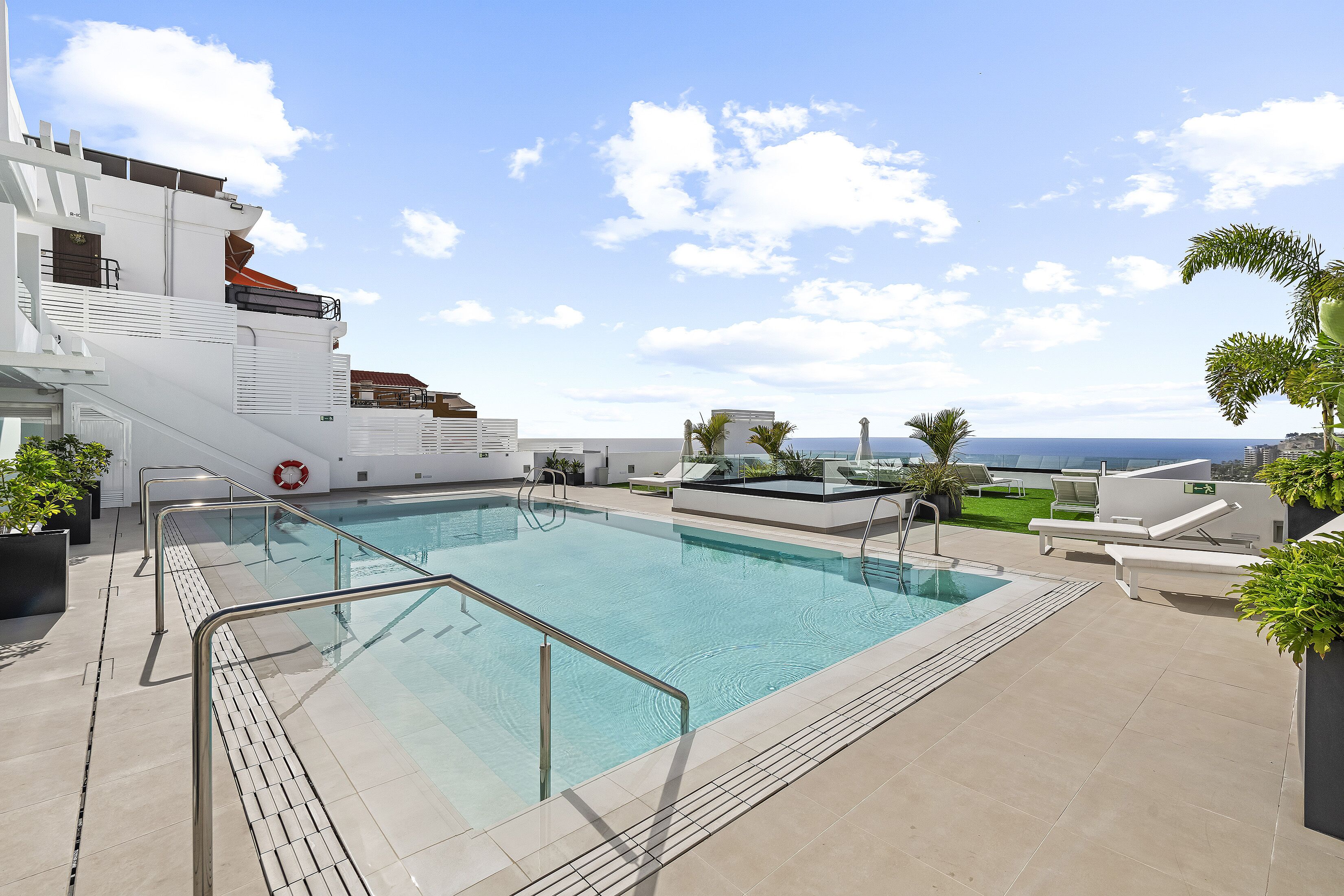 Ein Pool auf dem Dach mit freiem Blick auf den Ozean, umgeben von Liegestühlen und Topfpflanzen.