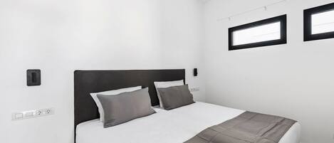 A modern bedroom with a large bed, two bedside tables, a wall-mounted light, and a window.