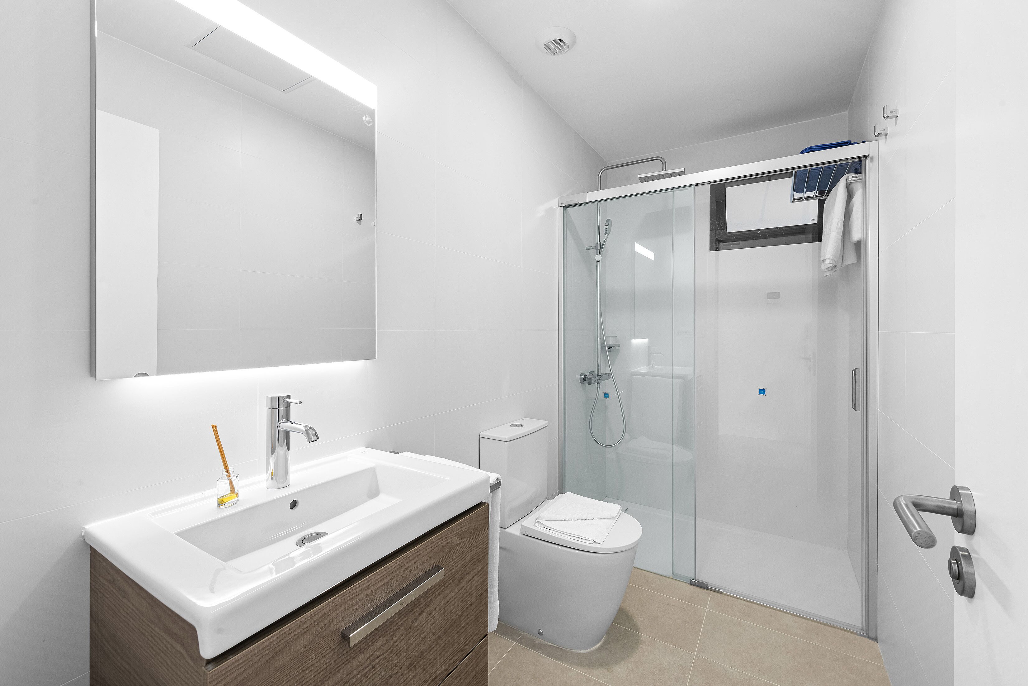 Ein modernes Badezimmer mit Duschkabine aus Glas, Waschbecken in Weiß mit Holzschrank und Toilette.