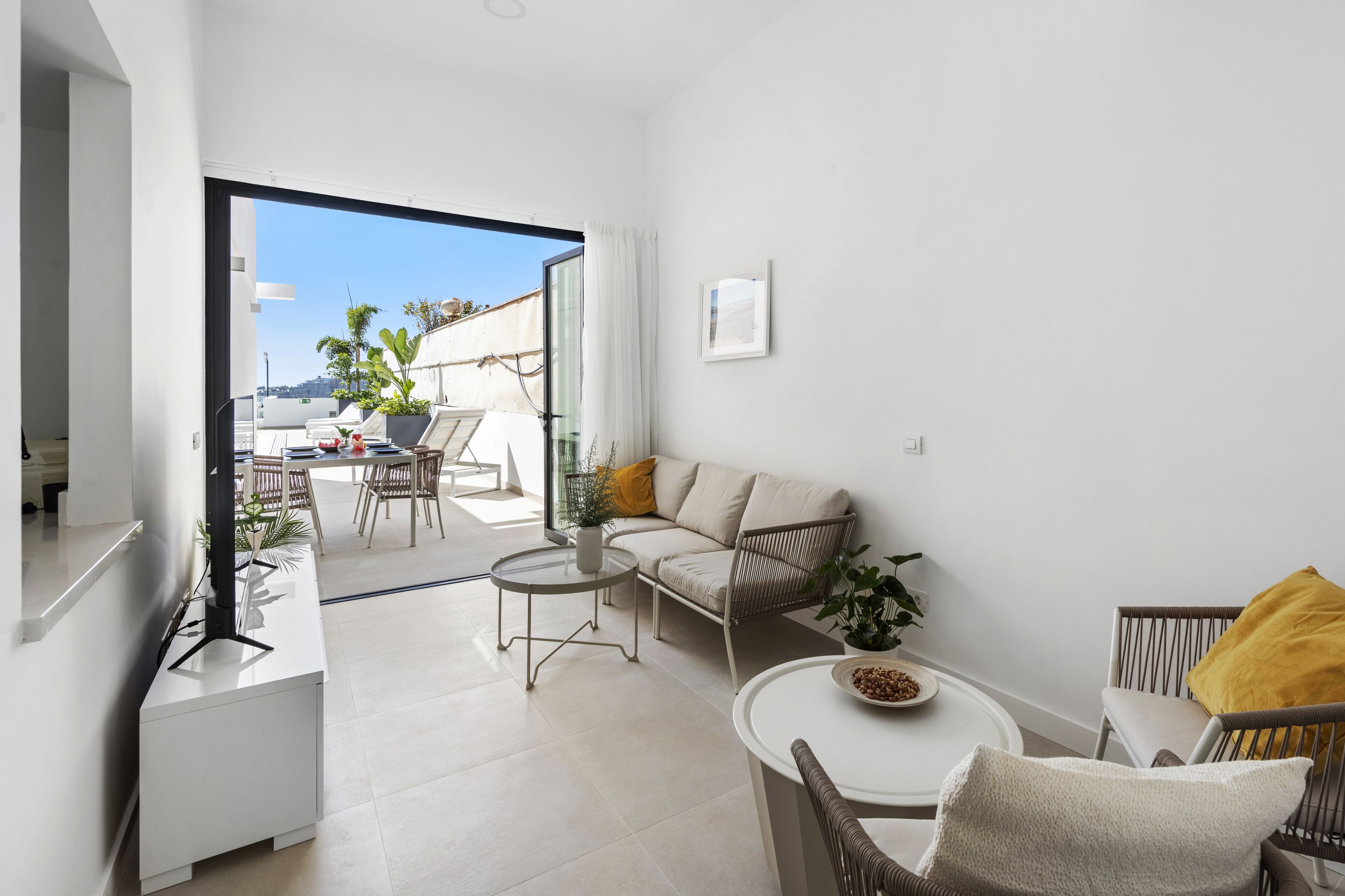 Un soggiorno moderno con un divano, due poltrone, un tavolino e una TV. Sul balcone, un tavolo e delle sedie, con vista sulla città.