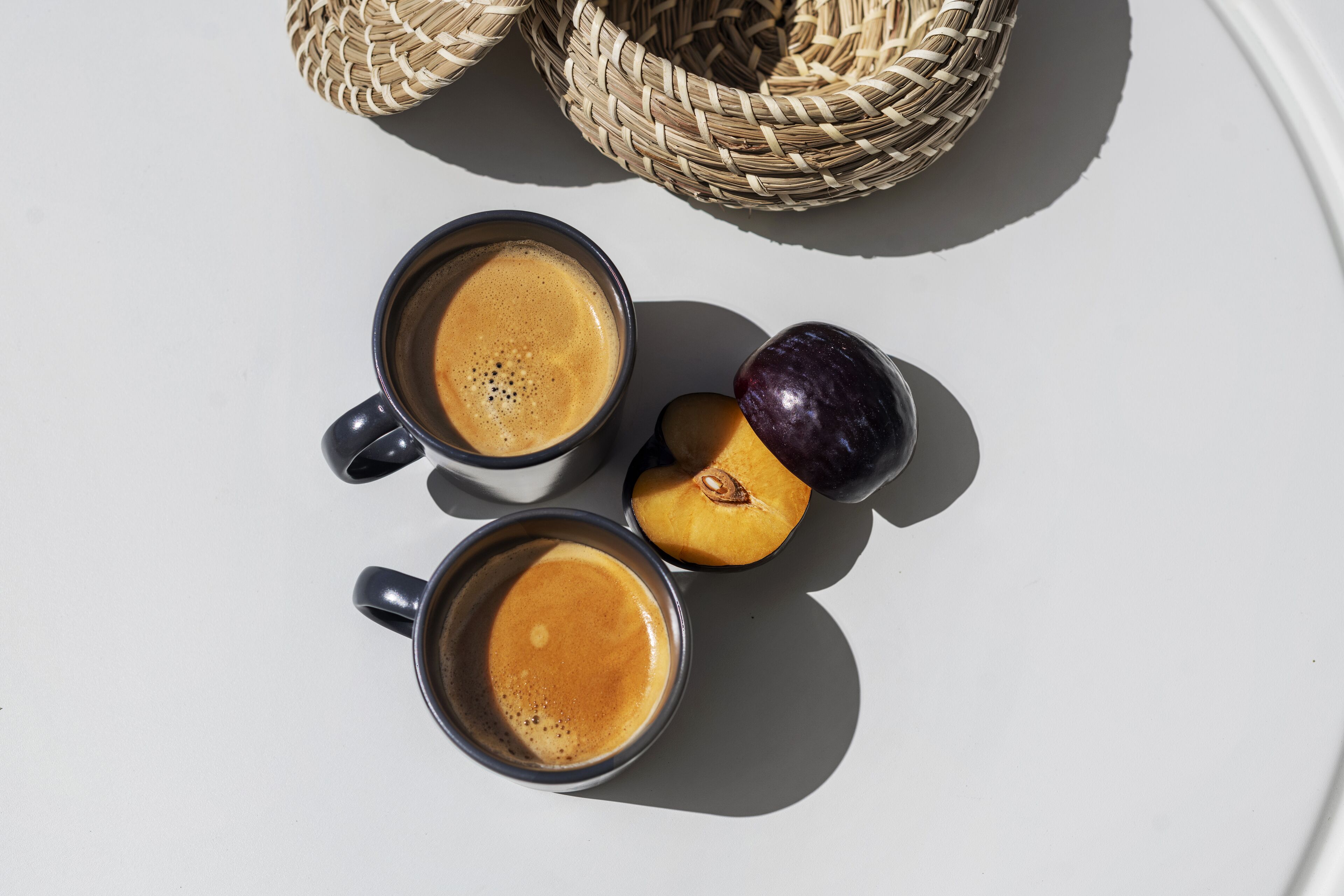 Two cups of coffee and two halves of a peach on a white surface.
