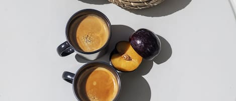 Two cups of coffee and two halves of a peach on a white surface.
