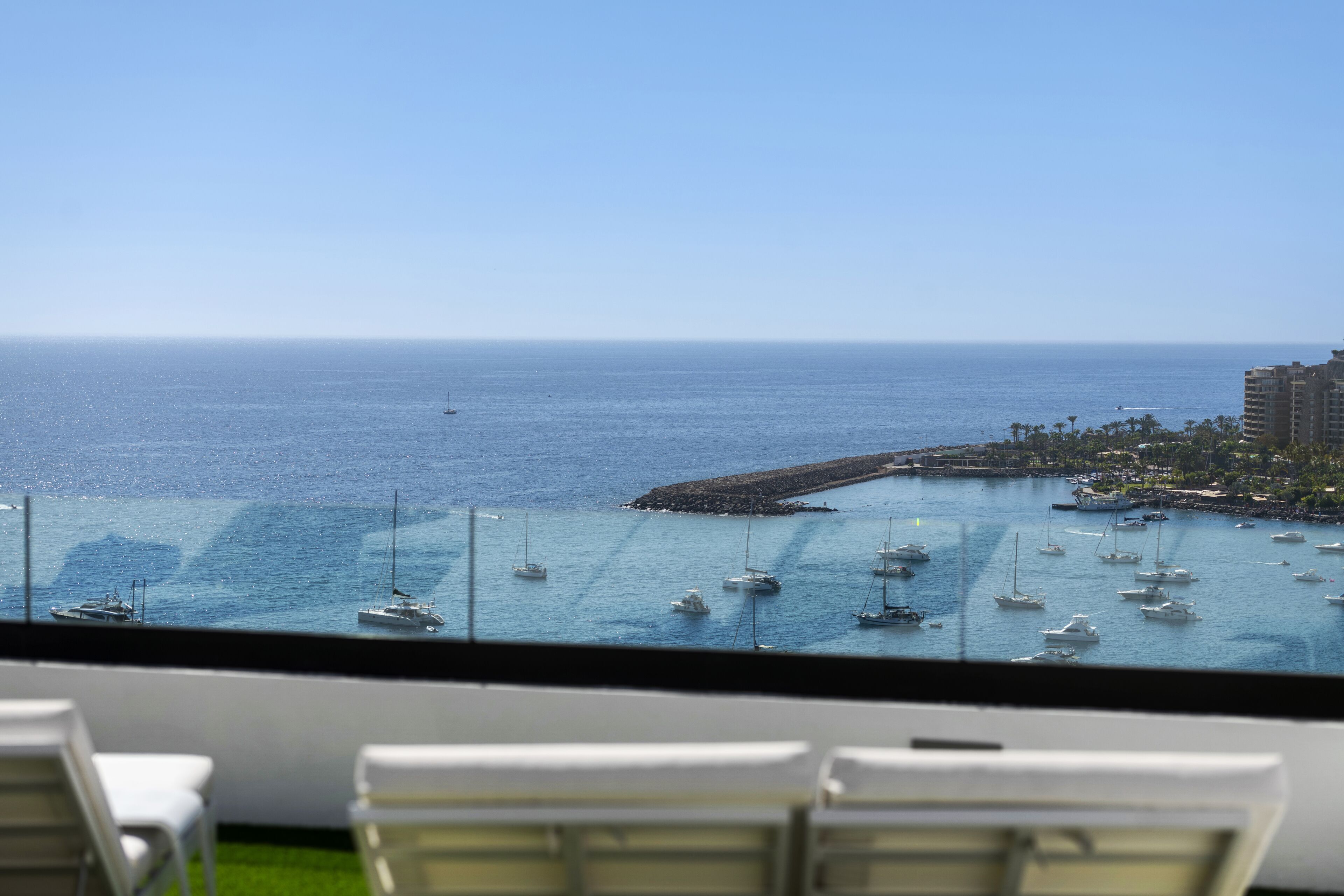 A view of a marina with multiple boats, a clear sky, and a distant shoreline with buildings.