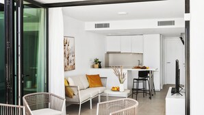 A modern living area with wicker furniture, a sofa, a dining table, and a kitchen in the background. - Palmera Sea View (Mogan)