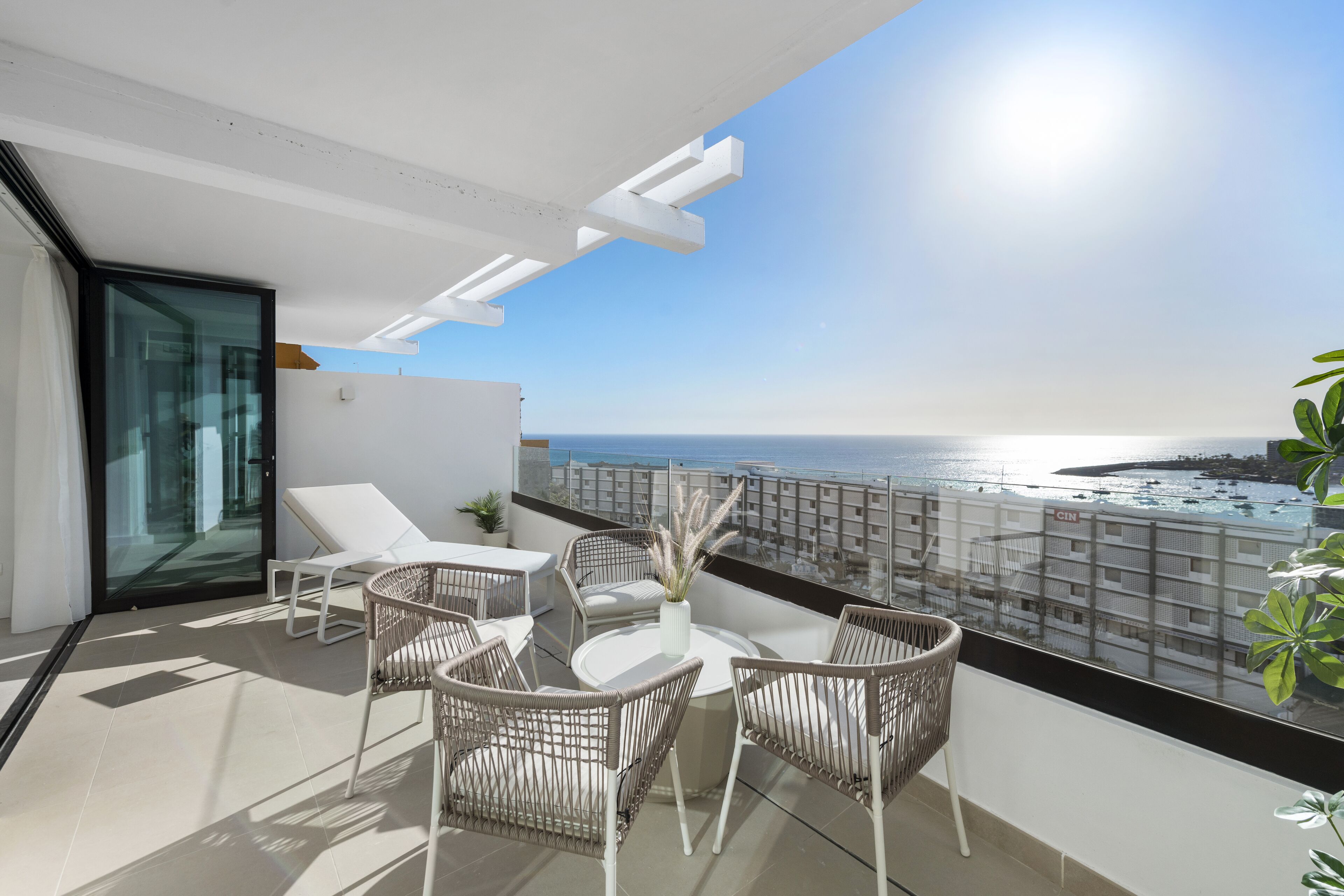 A balcony with a view of the sea, white furniture, and a glass door.
