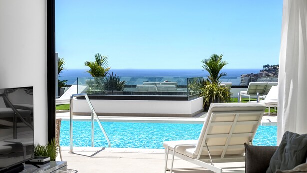 A modern hotel room with a large window overlooking a pool and the ocean. - Palmera Sea View (Mogan)