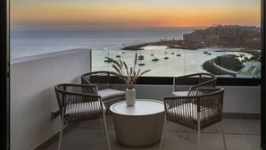 A balcony with wicker chairs and a table, overlooking a marina with boats and a coastal cityscape at sunset. - Palmera Sea View (Mogan)