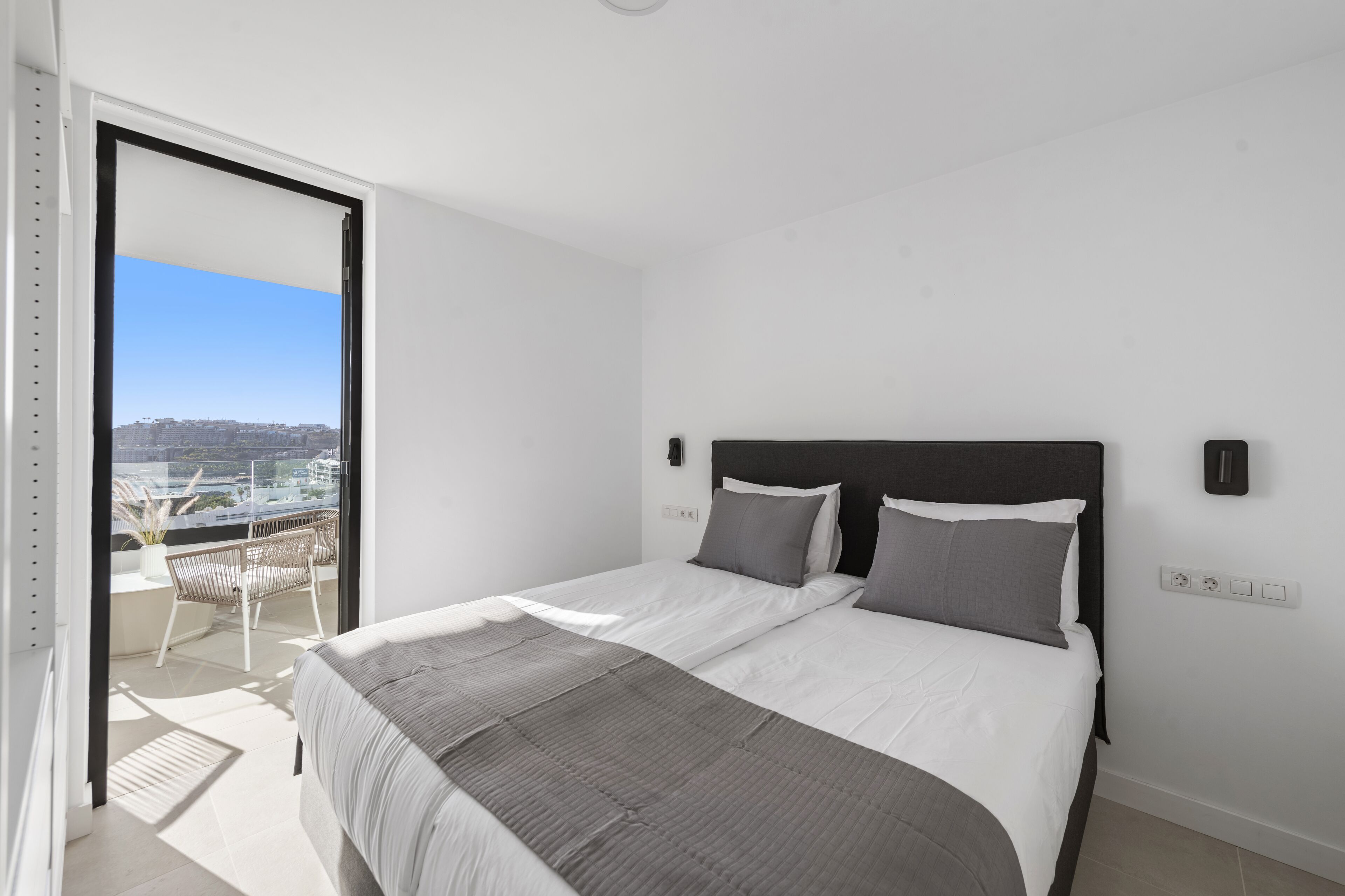 A modern bedroom with a large bed, a balcony with a view, and a cityscape in the background.