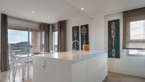 A modern kitchen with a central island, white cabinetry, and a large window offering a view. - ENJOYBCN MARINA APARTMENT (Barcelona)