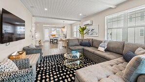 A modern living room with a sectional sofa, a glass coffee table, and patterned ottomans. - Canalfront! Pool, Dock, Near Anna Maria Island (Cortez)