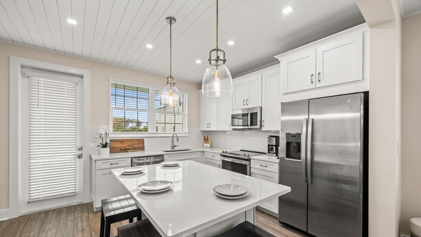 A modern kitchen with white cabinetry, stainless steel appliances, and a central island with stools. - Canalfront! Pool, Dock, Near Anna Maria Island (Cortez)