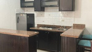 Una cocina compacta con armarios oscuros, un refrigerador, una estufa a gas y un lavamanos.