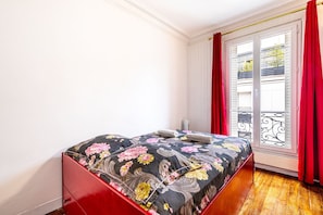 Een slaapkamer met een bed, een raam met rode gordijnen en een uitzicht op het balkon.
