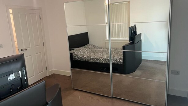 A bedroom with a mirrored wardrobe, a bed with patterned bedding, and a TV stand. - Immaculate 1-bed Apartment in East London (London)