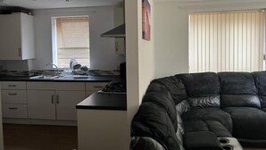 A modern kitchen with white cabinets, a black countertop, and a window with blinds. - Immaculate 1-bed Apartment in East London (London)
