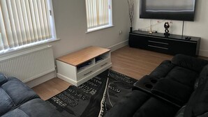 A modern living room with a flat-screen TV, a black sofa, a wooden coffee table, and a black rug. - Immaculate 1-bed Apartment in East London (London)
