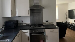 A modern kitchen with white cabinets, a stainless steel range hood, and a black countertop. - Immaculate 1-bed Apartment in East London (London)