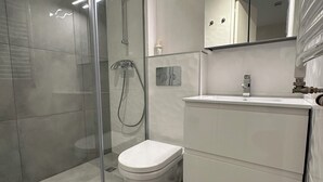 Et moderne badeværelse med en glasvægs brusekabine, et hvidt toilet og en vask med spejl.