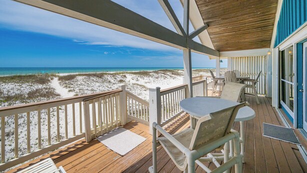 A wooden deck with a table and chairs overlooking a beach. - Conch Out 1405 | Gulf-Front Beach House (Gulf Shores)
