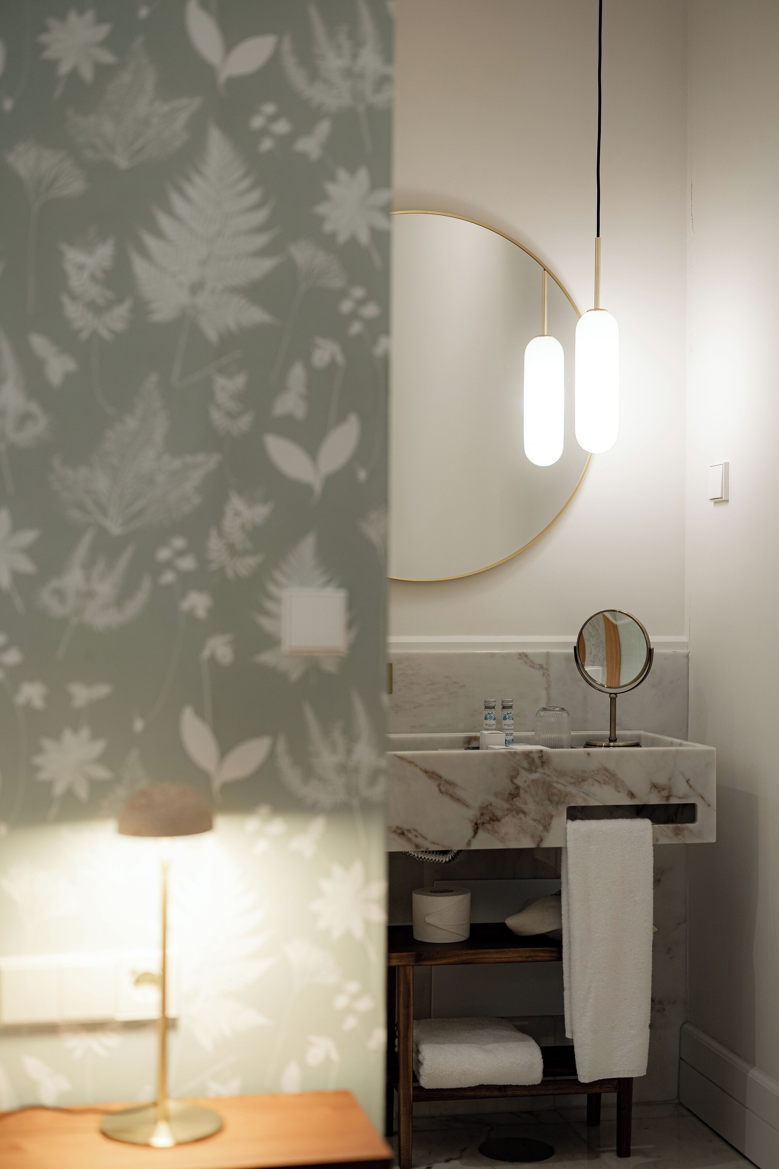 A bathroom with a marble sink, a round mirror, and a towel rack.