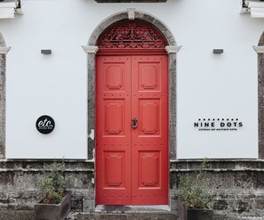 Une porte rouge à deux battants, surmontée d’une arche décorative, et de part et d’autre, deux enseignes : l’une pour « etc. Osteria Bar » et l’autre pour « Nine Dots Azorean Art Boutique Hotel ».