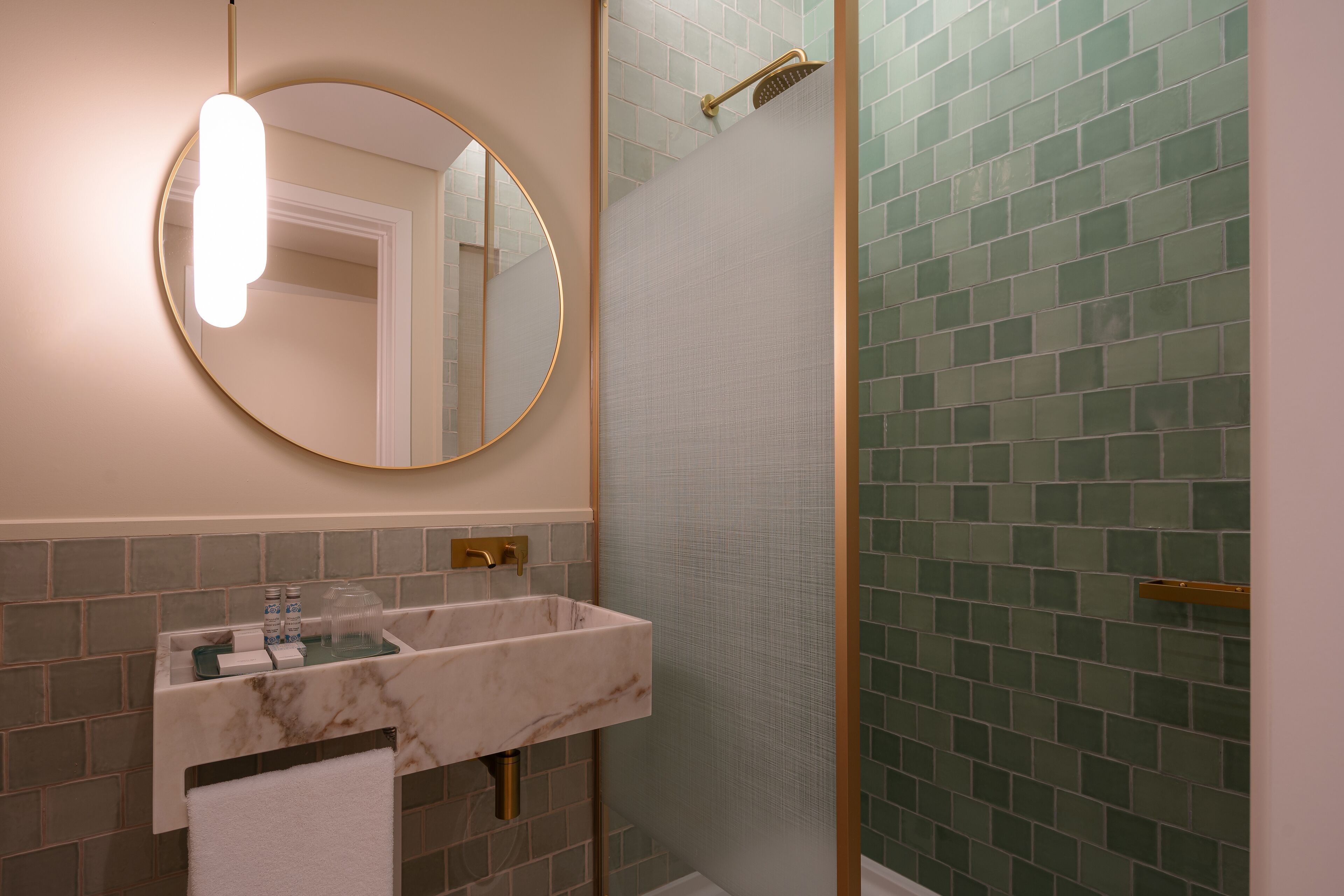 Un baño con lavamanos de mármol, un espejo redondo y una ducha con mosaicos verdes.